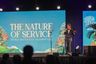 Un orador en el escenario frente a una pantalla que dice The Nature of Service, World Water Day Celebration