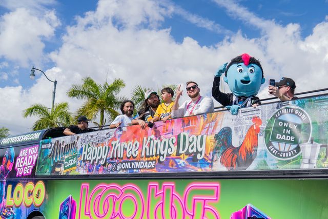 Parade guests and a mascot greeting the crowd from a bus