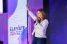 Speaker presenting on the Elevate Small Business stage beside the event logo