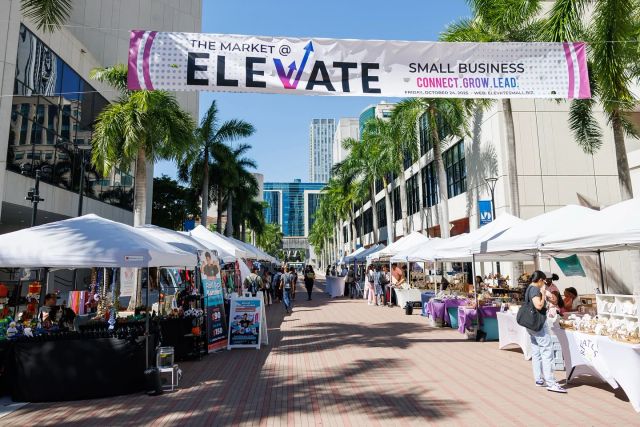 Outdoor vendor market beneath an Elevate Small Business banner in downtown Miami