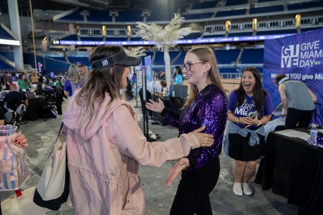 Two women greeting each other beside a Give Miami Day display